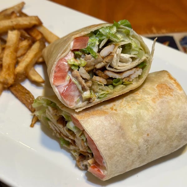 Two halves of a chicken wrap with lettuce, tomatoes, and sauce, served with french fries.