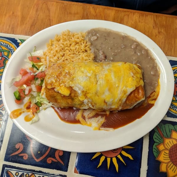 A Cafe Bueno burrito covered in melted cheese, with rice, refried beans, and pico de gallo.